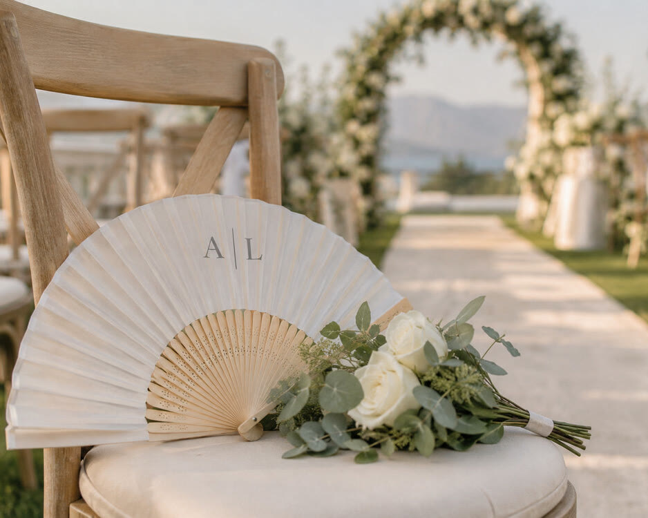 White bamboo hand fan with a printed monogram, on a wedding ceremony chair